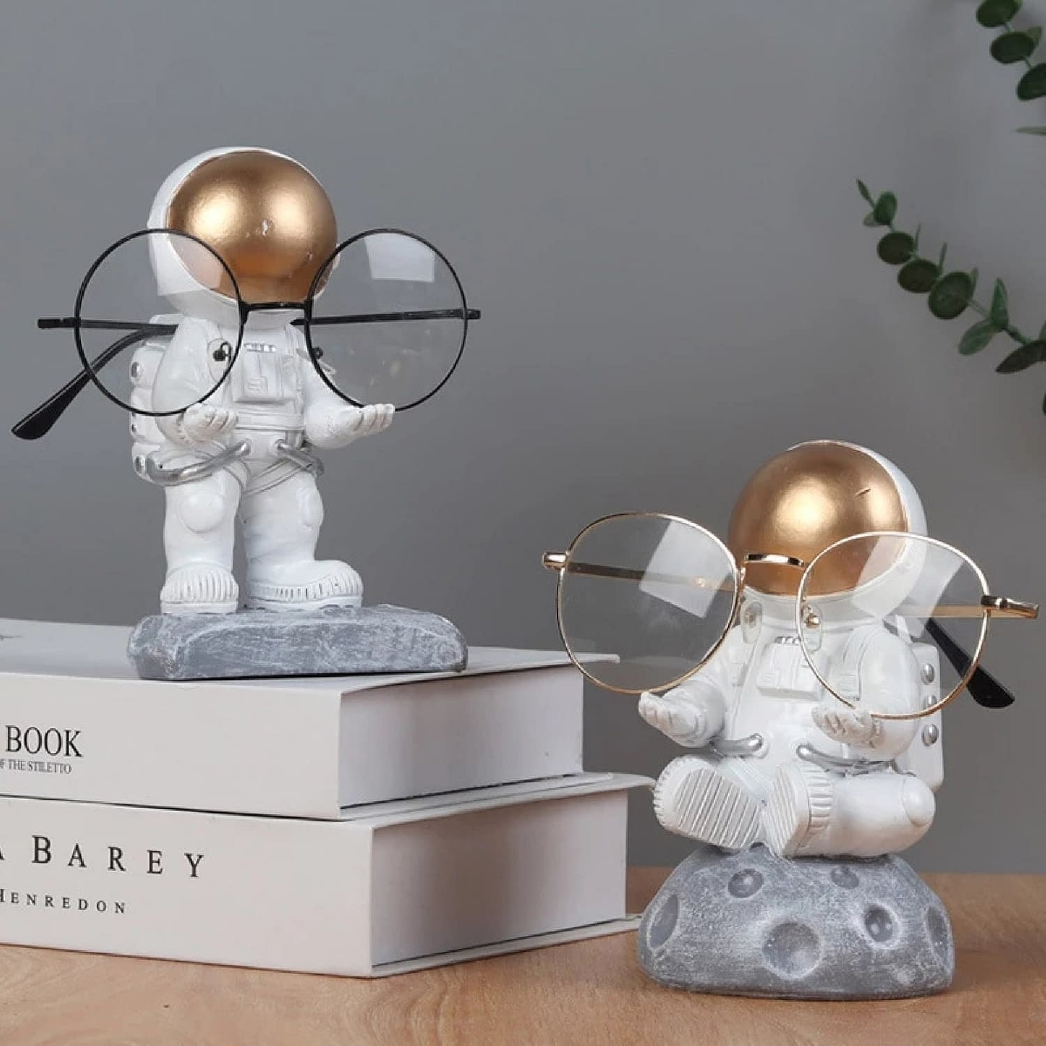 Two astronaut figures holding eye glasses standing on a desk and books.