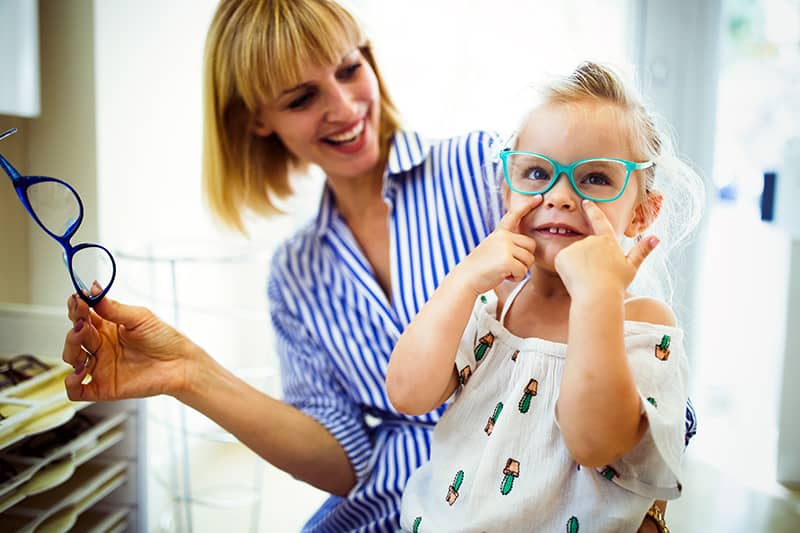 Happy mother with her little daughter choosing glasses