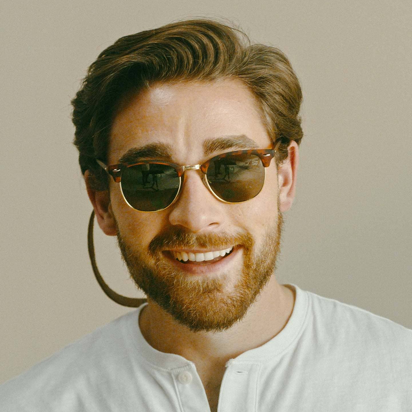 Man wearing sunglasses with leather sunglass strap and smiling at camera.