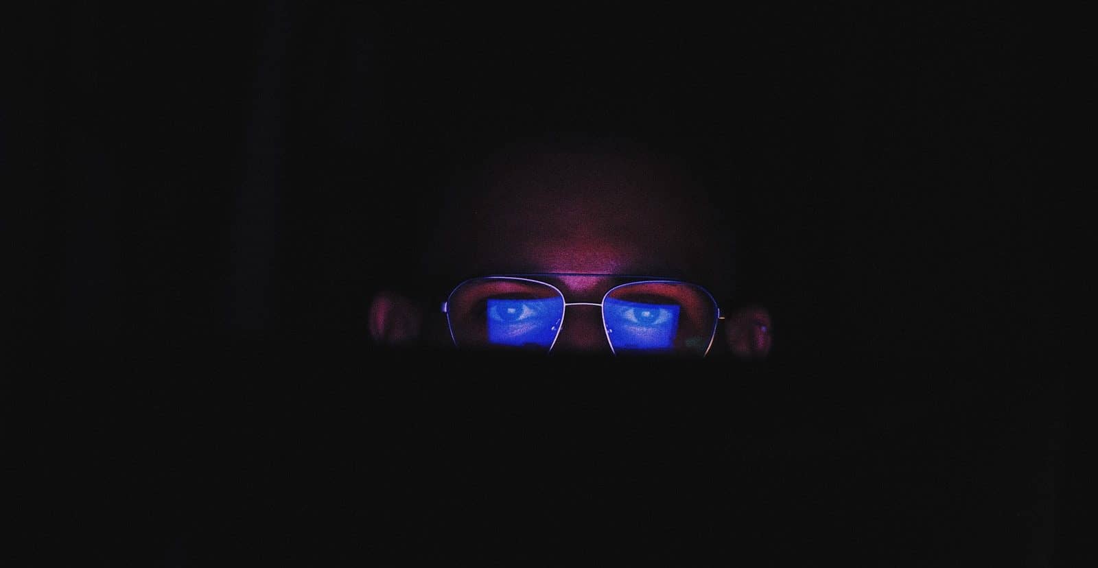 person in the dark with blue reflection on their glasses