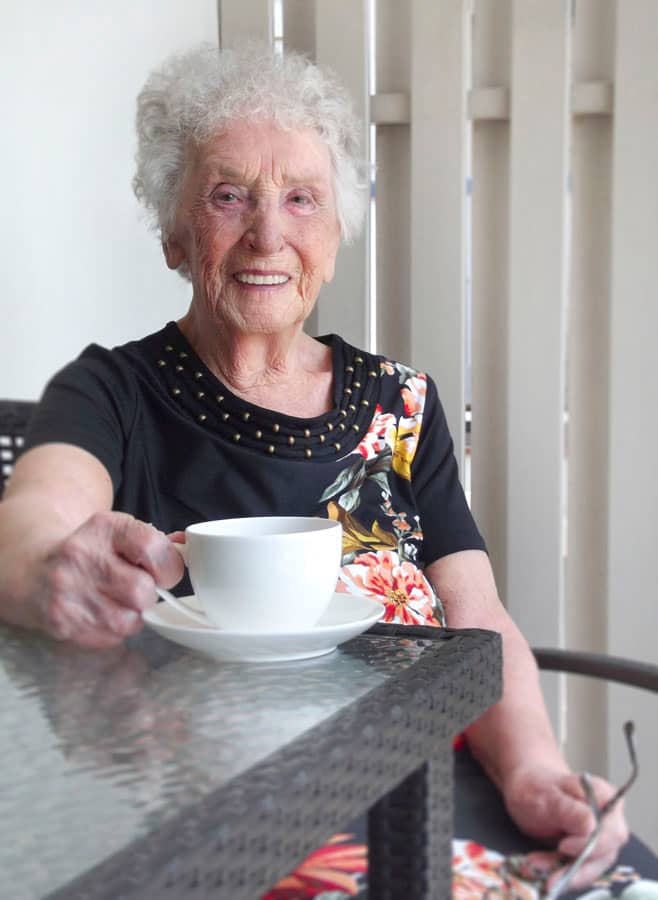 Smiling elderly lady drinking coffee on a patio outside her home